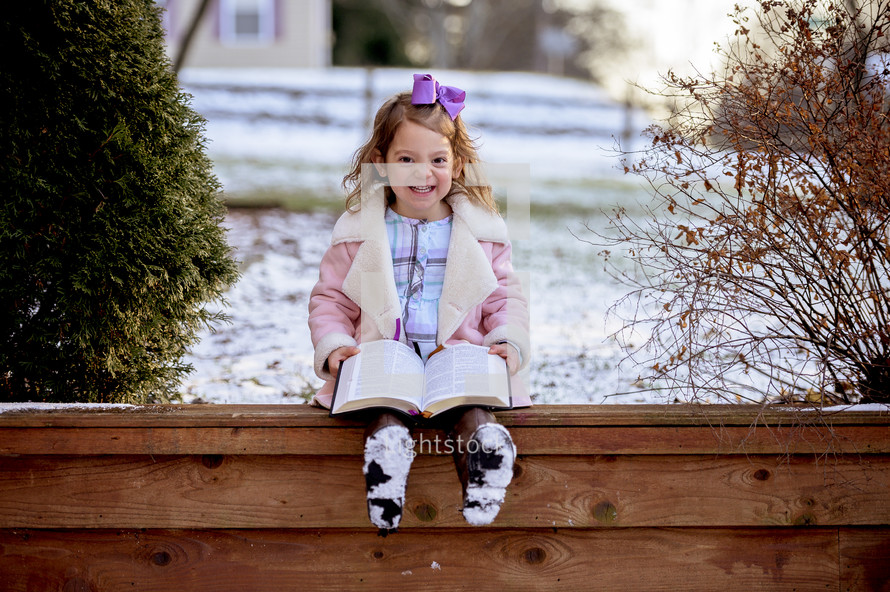 little girl reading a Bible outdoors in snow 