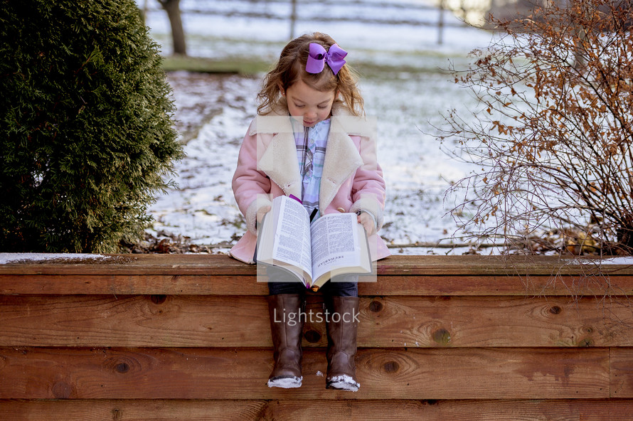 girl in a pink coat reading a Bible 