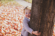 little girl playing in fall leaves and hugging a tree 