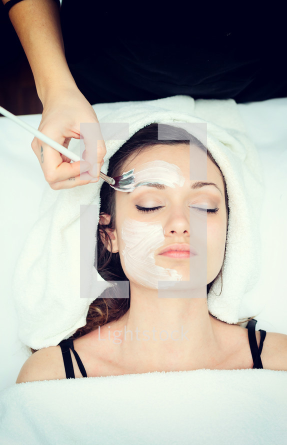Cosmetician applying facial beauty mask for young woman at spa salon