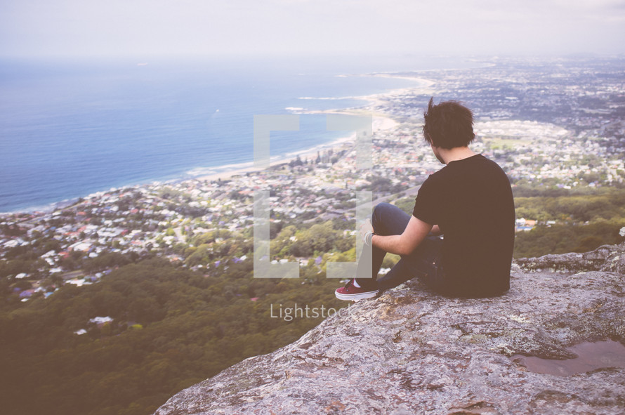 A man sitting at the edge of cliff looking out 