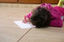 a child drawing on paper on the floor 