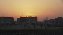 Sun setting behind buildings and homes in city of Dubai in suburban housing area.