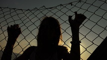 Woman holding onto a wire fence.