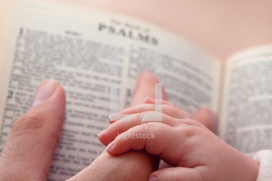 baby's hand holding Dad's finger over an open Bible