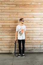 Man in sunglasses standing outside holding a skateboard.