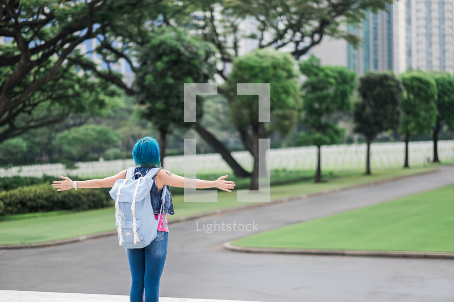 a woman with blue hair standing in a city with outstretched arms 