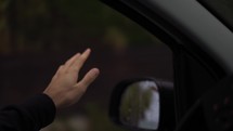 A man's hand is catching the rain out while driving a car on a rainy day, slow motion.