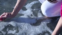 woman scooping up ocean water with her hands 