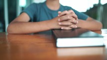 Close up hands praying on Bible at wooden table in morning