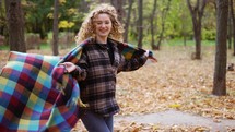 Curly girl in golden autumn park covering herself in plaid spinning around and smiling.