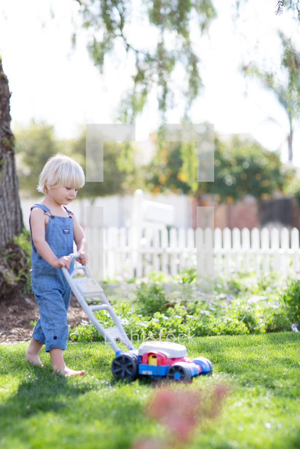Little boy in overalls mowing the yard. 