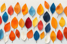 Colorful array of abstract autumn leaves in shades of orange, red, yellow, and blue arranged on a textured white background. A vibrant and modern representation of the fall season.