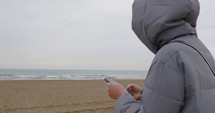 Woman in a coat on a phone at the beach