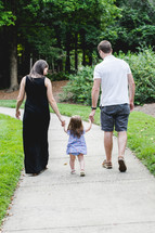 a mother and father walking holding hands with their daughter 