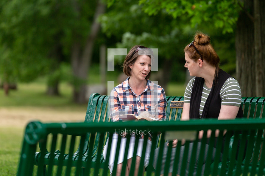 Two women sitting on a bench in the park studying the Bible