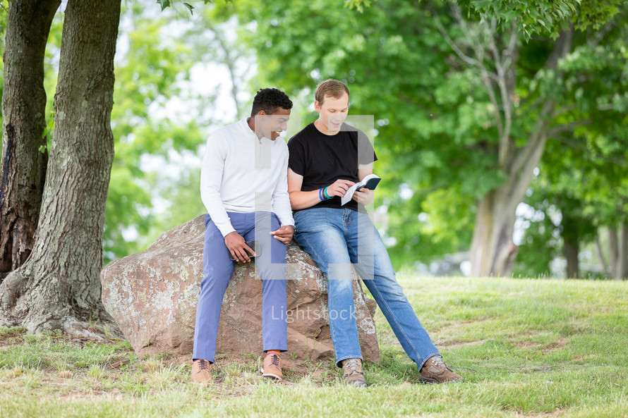 Guys sitting on a rock reading the Bible