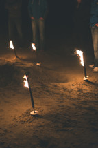 People standing around burning torches in the ground.