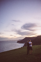 couple hugging and looking out at a coastline 