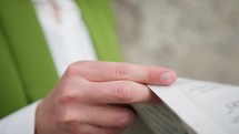 Close up of a woman in a green blazer's hands holding a newspaper.