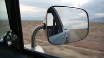 rearview mirror view as a car drives on a desert road 