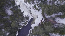 Aerial drone view of a frozen waterfall nestled in a wintry forest landscape surrounded  by trees