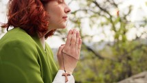 Woman praying holding a cross surrounded by trees.