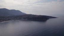 Aerial Over Calm Ionian Sea With Himare Coastline And Mountains In Background In Albania. Slow Pan Left, Establishing Shot