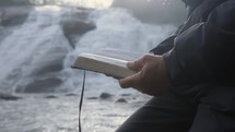 a man standing in front of a waterfall reading a Bible 