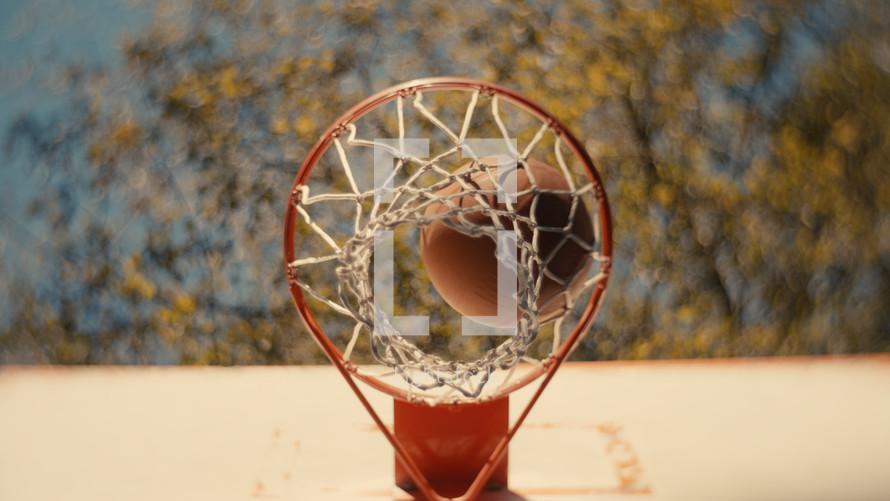 Close up of a basketball being shot on an outdoor basketball court on a sunny day