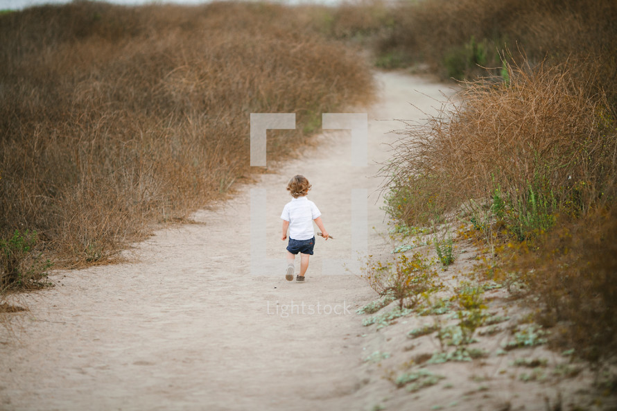 toddler standing on a sandy path 