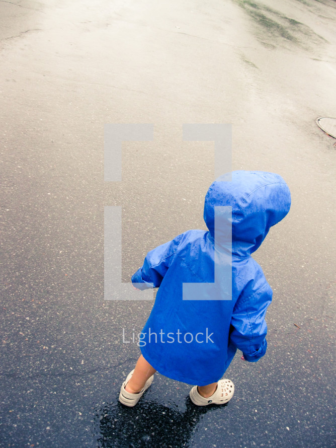 toddler in a raincoat on wet pavement 