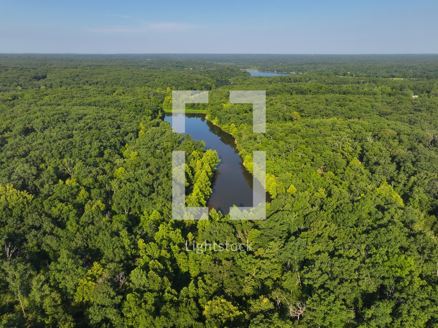 Drone view of two small lakes surrounded by green trees in the woods.