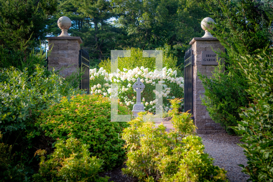 Cross monument and gate between stone pillars at the entrance of an Irish Garden 