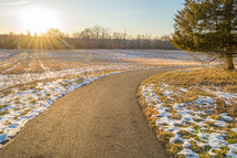 snow on grass and a paved path 