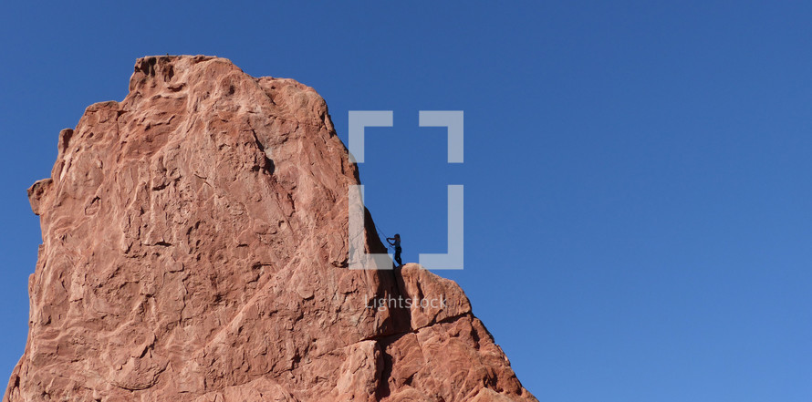 rock climber on rugged red rock against blue sky