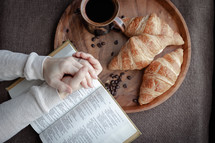 praying hands over a Bible and coffee and croissants 
