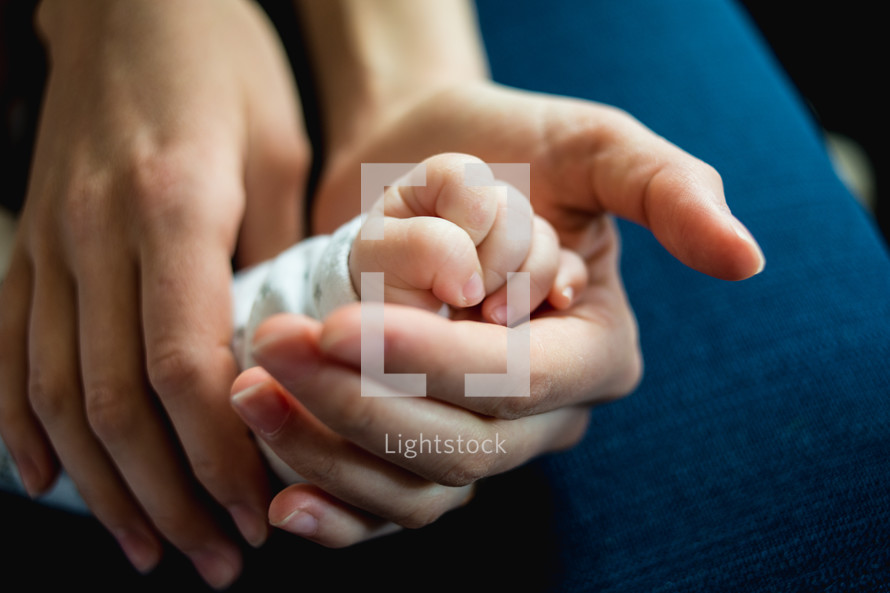 a mother holding a newborns hand 