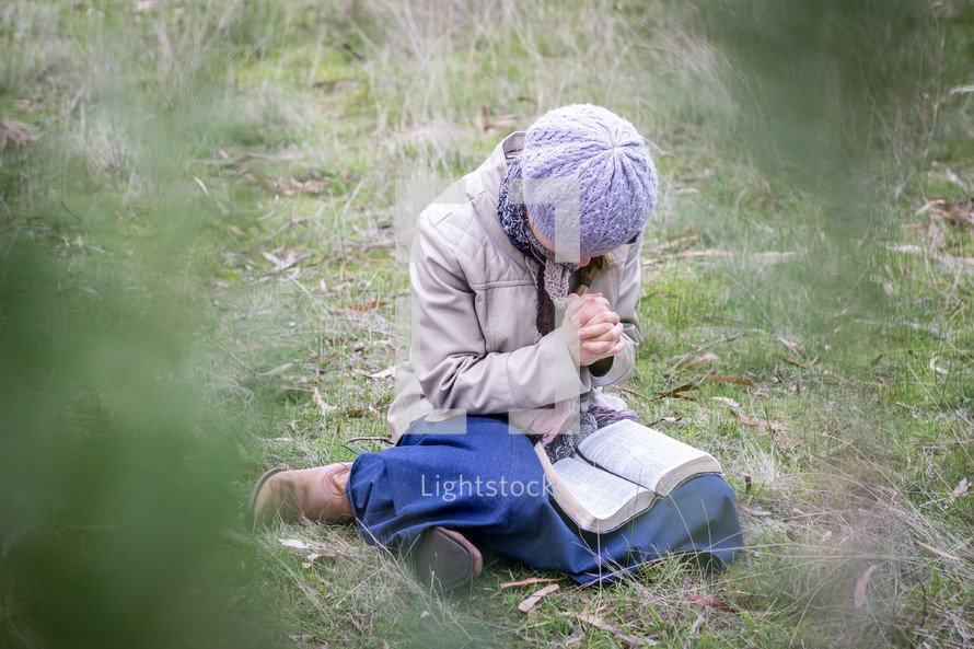 a girl praying over a Bible in her lap 