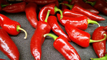 A group of red shiny peppers draw the eye and reflect light in the produce stand to attract the eye and show it is good to eat. Spicy, hot food ideal for the summer time or to add to barbecues, tacos or salads.