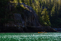 Kayakers paddling in a fjord lined with cliffs and trees