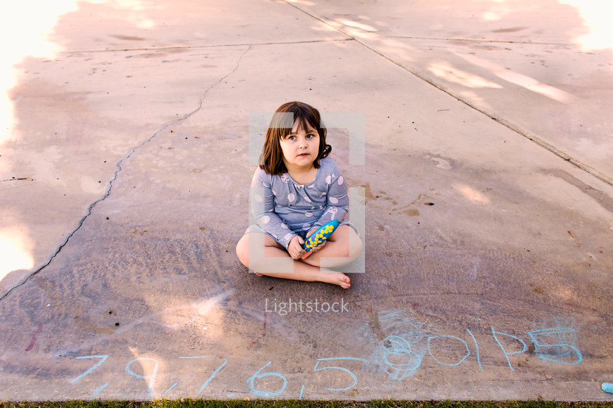 a child sitting on concrete next to chalk drawings 