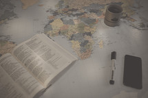 open Bible, marker, cellphone and coffee mug on a world map 