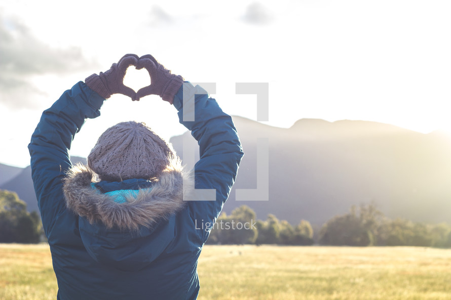 a woman standing outdoors in winter making a heart with her hands 