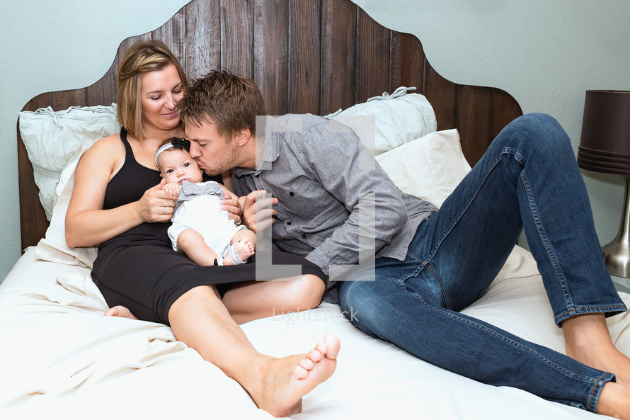 mother and father in bed with their infant daughter 