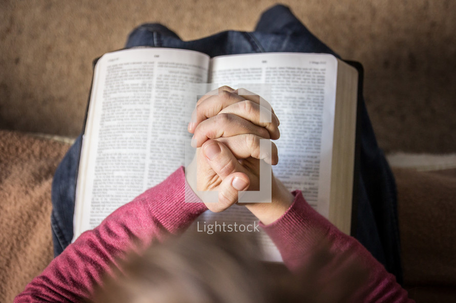 praying hands over an opened Bible 