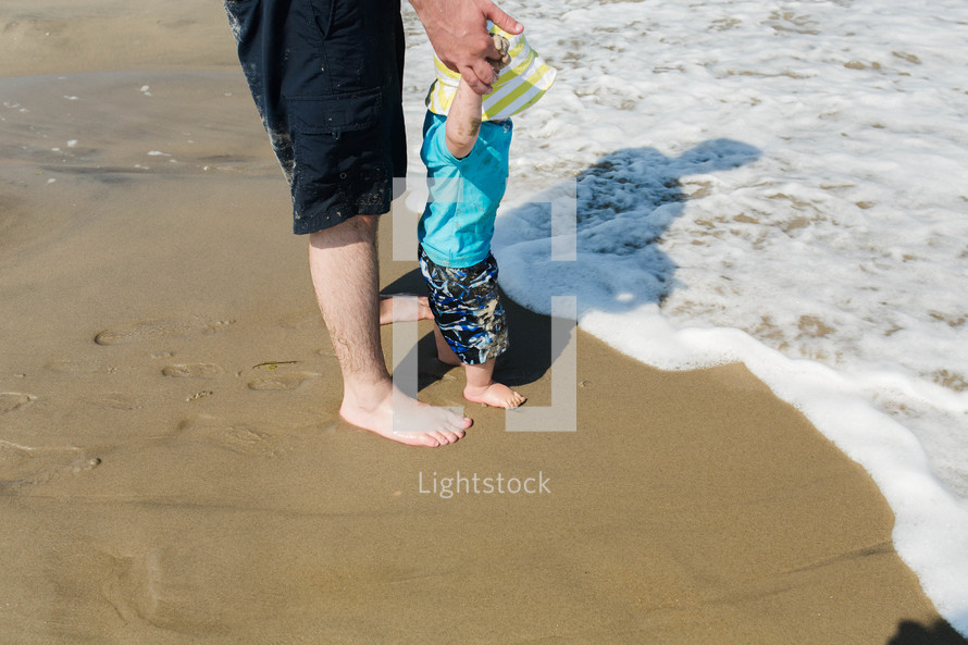 a father walking with his toddler son on a beach 