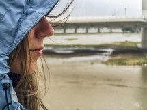 A woman's face in a rain coat near the ocean.