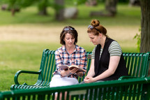 Two women studying the Bible on a park bench