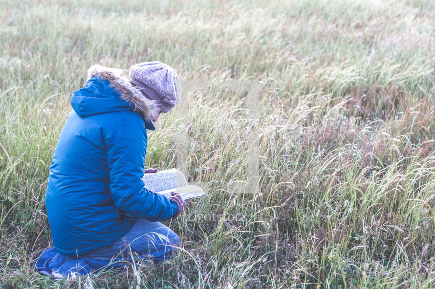 a woman kneeling in a field reading a Bible 